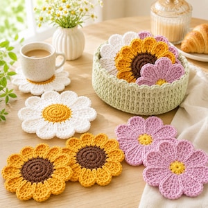 May include: A set of crocheted flower-shaped coasters in white, yellow, brown, and purple, stored in a round, light green crocheted basket. The coasters feature detailed petal designs and circular centers, with some placed individually and others stacked inside.