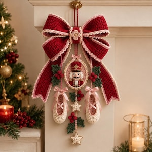 Op de afbeelding: Een decoratieve wandhanger met een grote, donkerrode gehaakte strik met lichtroze rand. Aan de strik hangt een centraal ovaal frame met een gehaakte notenkraker, geflankeerd door twee kleine crèmekleurige balletschoentjes met roze linten.