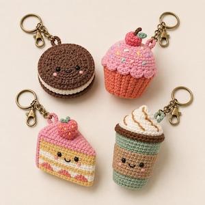 May include: Four crocheted keychains shaped like food items: a brown sandwich cookie, a pink cupcake with sprinkles, a slice of strawberry cake, and a green coffee cup with whipped cream. Each item features a smiling face and a bronze metal keyring.