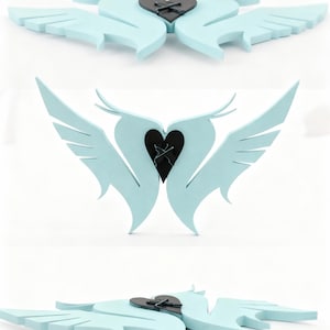 Puede incluir: Decoración de pared en forma de corazón azul claro con alas estilizadas. El centro presenta un corazón negro con un diseño cosido. Las alas están compuestas por múltiples capas, creando un efecto en capas. La decoración probablemente está hecha de espuma o un material similar.