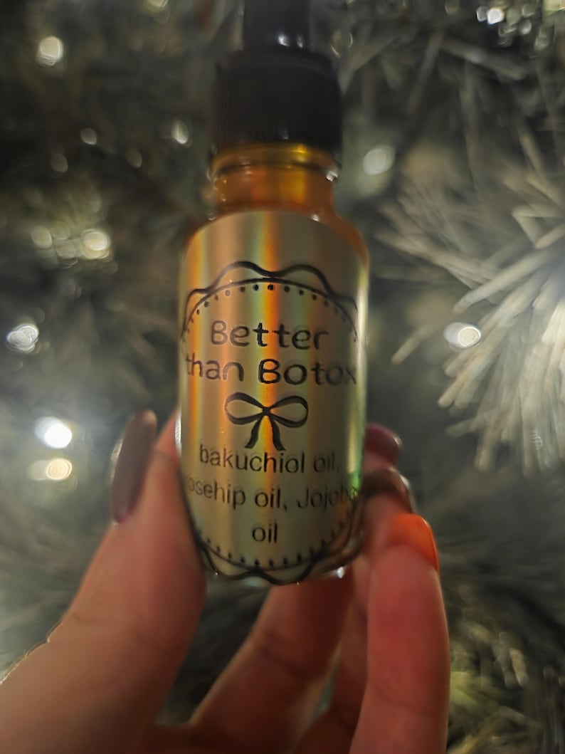 May include: A small amber glass bottle with a black dropper top. The label reads "Better than Botox" with a bow graphic, and lists bakuchiol, rosehip, and jojoba oils. The bottle is held against a blurred background.
