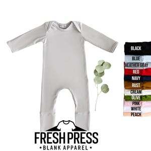 May include: A light gray baby jumpsuit with long sleeves and attached feet. The jumpsuit is displayed with a color chart showing various colors, including black, blue, and pink. The brand logo "FRESH PRESS BLANK APPAREL" is at the bottom.