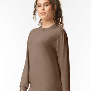 May include: A long-sleeved, crew neck shirt in a solid brown color. The shirt has a simple, classic design with a ribbed cuff at the wrist. The fabric appears to be a soft, comfortable material, suitable for casual wear.
