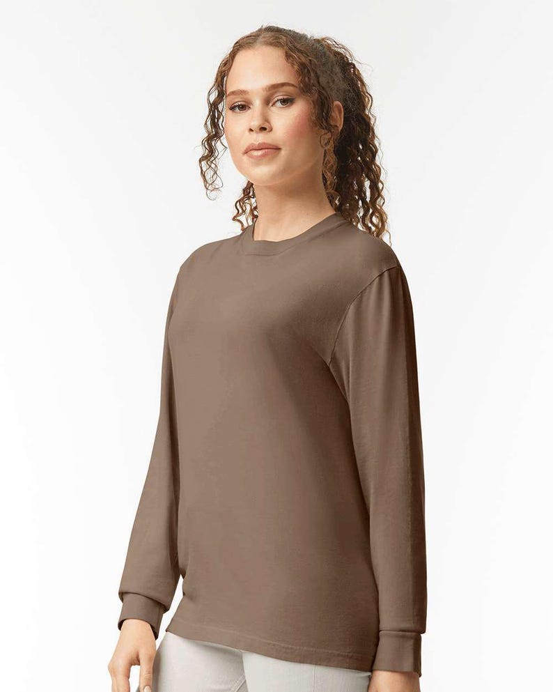 May include: A long-sleeved, crew neck shirt in a solid brown color. The shirt has a simple, classic design with a ribbed cuff at the wrist. The fabric appears to be a soft, comfortable material, suitable for casual wear.