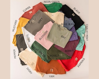 May include: A collection of crew neck t-shirts in various colors, including mustard, grey, and black. Each shirt has a tag with the color name, such as "Blossom" and "Bay". The shirts are arranged in a circular pattern.