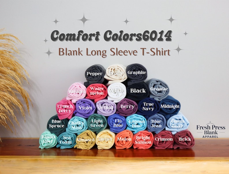 May include: A display of rolled-up Comfort Colors 6014 blank long sleeve t-shirts in various colors, including black, white, and blue. The image features the text "Comfort Colors 6014 Blank Long Sleeve T-Shirt" and the Fresh Press Blank Apparel logo.