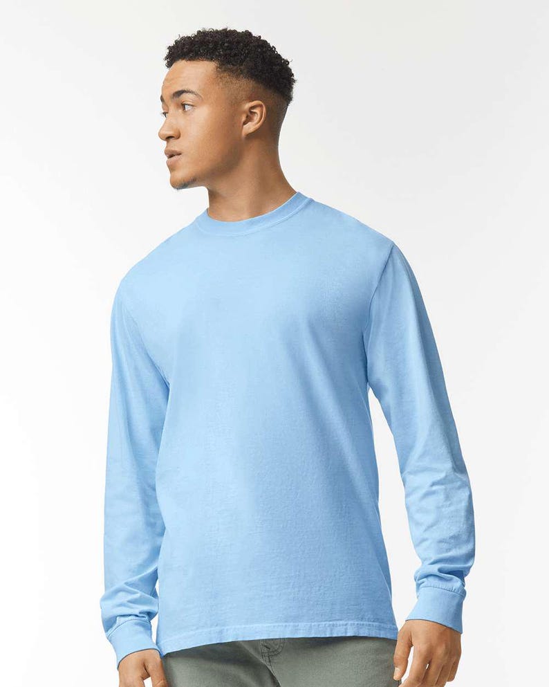 May include: A light blue long-sleeve t-shirt. The shirt has a crew neck and long sleeves with ribbed cuffs. The fabric appears to be a soft, solid color. The shirt is a casual style.