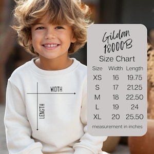 May include: A cream-coloured sweatshirt with a size chart graphic. The chart, labelled "Gildan 18000B," lists sizes XS to XL with width and length measurements in inches. The sweatshirt has a crew neck and long sleeves.