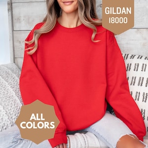 May include: A bright red crewneck sweatshirt. The sweatshirt is a solid color and has the text "ALL COLORS" on a brown label. The tag on the upper right corner says "GILDAN 18000".