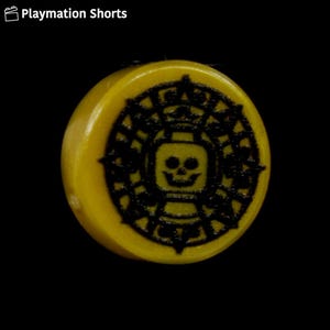 Könnte beinhalten: Ein gelbes, kreisförmiges Objekt mit einem schwarzen, detaillierten Design, das einen Totenkopf und eine Krone zeigt. Das Design erinnert an ein Piraten-Thema. Das Objekt befindet sich vor einem schwarzen Hintergrund. Der Text "Playmation Shorts" befindet sich in der oberen linken Ecke.