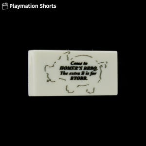 May include: A rectangular, off-white sign with the text "Come to HOMER'S BBQ. The extra B is for BYOBB," inside a pig outline. The sign is set against a black background.