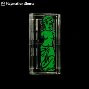 May include: A clear, rectangular block with a green illustration of a classical statue. The statue is depicted in a stylized, graphic manner. The text "Playmation Shorts" is in the upper left corner.