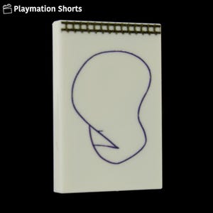 Può includere: Un blocco note rettangolare bianco sporco con un contorno blu di un volto e un piccolo triangolo. Il bordo superiore presenta un motivo strutturato marrone. Le parole "Playmation Shorts" sono nell'angolo in alto a sinistra.