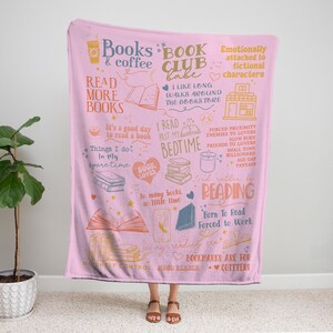 May include: A pink throw blanket with a book-themed design. The blanket features illustrations of books, coffee cups, and text like "Books & Coffee" and "Read More Books." The design includes phrases about reading and book lovers.