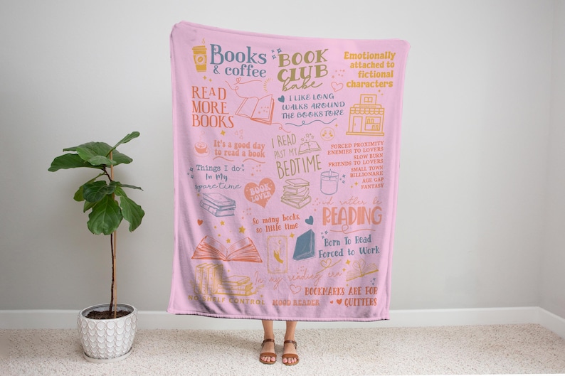 May include: A pink throw blanket with a book-themed design. The blanket features illustrations of books, coffee cups, and text like "Books & Coffee" and "Read More Books." The design includes phrases about reading and book lovers.