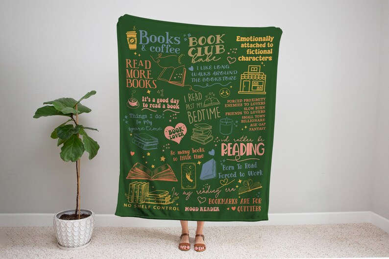 May include: A dark green throw blanket with book-themed illustrations and text. The blanket features phrases like "Read More Books," "Book Club Babe," and "I'd rather be reading." It includes drawings of books, coffee cups, and hearts.