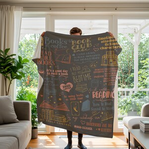 May include: A dark gray throw blanket with book-themed illustrations and text in various colors. The blanket features phrases like "Books & coffee," "Book Club Babe," and "I read past my bedtime." It's a cozy item for book lovers.