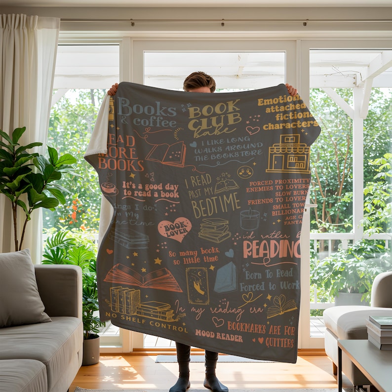 May include: A dark gray throw blanket with book-themed illustrations and text in various colors. The blanket features phrases like "Books & coffee," "Book Club Babe," and "I read past my bedtime." It's a cozy item for book lovers.