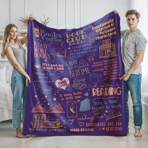 May include: A purple fleece blanket with various book-themed illustrations and phrases in white and orange. The blanket features text such as "Books & Coffee," "Book Club Babe," and "I'd rather be reading."