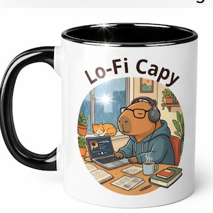 Può includere: Tazza in ceramica bianca con manico e bordo neri. La tazza presenta un'illustrazione a cartoni animati di un capibara con cuffie e occhiali, che lavora su un laptop. Il testo "Lo-Fi Capy" è stampato sulla tazza, insieme alle parole "Durable ORCA coating".