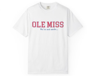 May include: White t-shirt with the text "OLE MISS" in red and blue block letters. Below the text is the phrase "We're not snobs..." in a smaller font. The shirt has a crew neck and short sleeves.