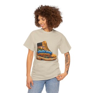 Puede incluir: Camiseta beige con un gráfico de una bota de trabajo con el texto "South Side Certified". El diseño de la bota incorpora imágenes del horizonte de la ciudad y los números "312" y "773". La camiseta la lleva una persona.