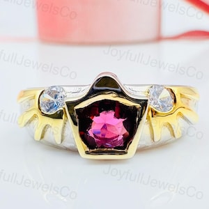 May include: A two-tone ring with a central, faceted, pink gemstone in a gold setting. The ring has a silver band with gold accents and two clear, round gemstones on either side of the central stone. The ring is displayed on a white surface.