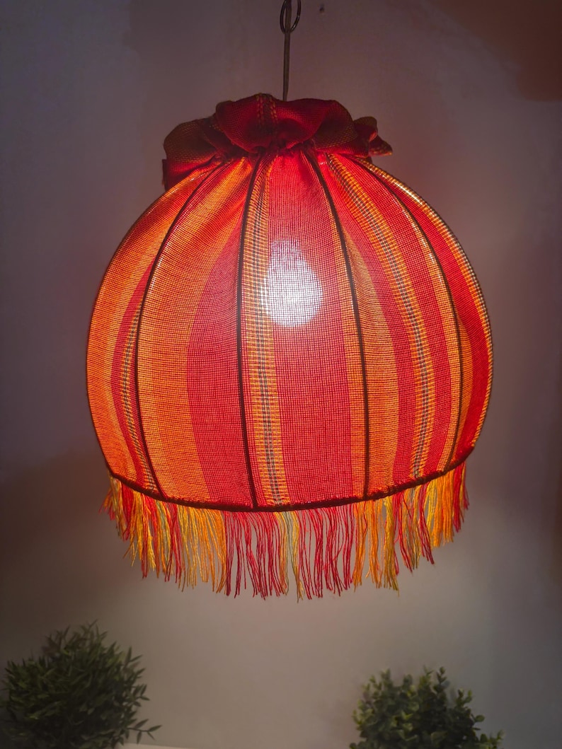Peut inclure: Suspension luminaire avec abat-jour rond ray&eacute; rouge et orange. L'abat-jour est orn&eacute; d'une frange en bas et est suspendu &agrave; une cha&icirc;ne m&eacute;tallique. La lampe est &eacute;clair&eacute;e de l'int&eacute;rieur.