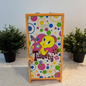 May include: A small, orange metal locker with a colorful design featuring Tweety Bird. The locker has a key lock and is decorated with polka dots, flowers, and a butterfly. The word "Tweety" is written on the front.