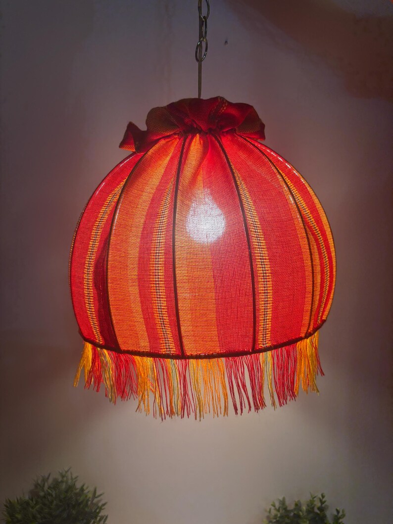 Peut inclure: Suspension luminaire avec abat-jour ray&eacute; rouge et orange. L'abat-jour est de forme arrondie, avec une frange en bas et un sommet fronc&eacute;. La lampe est suspendue &agrave; une cha&icirc;ne.