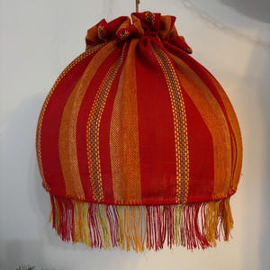 Peut inclure: Un abat-jour suspendu avec un motif &agrave; rayures rouges et oranges. L'abat-jour a un dessus fronc&eacute; et une bordure &agrave; franges en bas. L'abat-jour est suspendu &agrave; une cha&icirc;ne m&eacute;tallique.