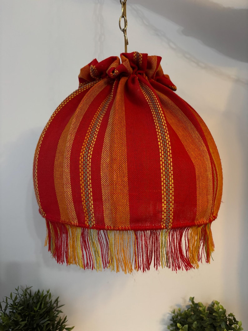 Peut inclure: Un abat-jour suspendu avec un motif &agrave; rayures rouges et oranges. L'abat-jour a un dessus fronc&eacute; et une bordure &agrave; franges en bas. L'abat-jour est suspendu &agrave; une cha&icirc;ne m&eacute;tallique.