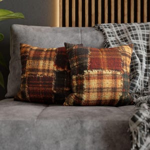 Könnte beinhalten: Zwei quadratische Dekokissen mit einem Patchwork-Karomuster in den Farben Dunkelrot, gebranntes Orange, Dunkelbraun und Senfgelb. Der Stoff hat eine strukturierte, gewebte Optik mit sichtbaren Linien, die ein gitterartiges Muster bilden.