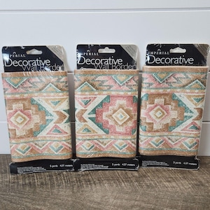 May include: Three rolls of decorative wall border with a Southwestern geometric pattern in shades of pink, teal, tan, and brown. Each roll is labeled "Imperial Decorative Wall Border". Each roll is 5 yards long.