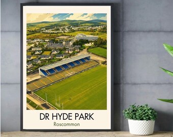May include: A framed poster featuring an aerial illustration of Dr. Hyde Park stadium in Roscommon, Ireland. The image shows a green sports field, a grandstand with blue seating, surrounding buildings, and rolling hills under a blue sky.
