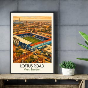 May include: A framed art print of Loftus Road stadium in West London. The artwork depicts the stadium with a green field, blue seating, and surrounding buildings under a warm sunset sky. The text "LOFTUS ROAD West London" is at the bottom.