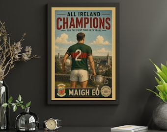 May include: A framed poster featuring a Gaelic football player in a green and red jersey with the number 2, holding a ball and a trophy. The text reads ALL IRELAND CHAMPIONS FOR THE FIRST TIME IN 75 YEARS and MAIGH EO, with a landscape background.