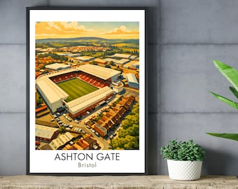 May include: A framed print of Ashton Gate stadium in Bristol. The artwork shows the stadium with a green pitch, red seating, and white structures. The sky is a mix of yellow and blue. The text "ASHTON GATE Bristol" is at the bottom of the print.
