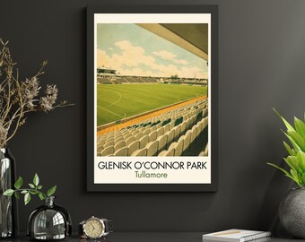 May include: A framed vertical art print depicting a stadium with a green field and rows of yellow and white seating under a blue sky with clouds. The text GLENISK O'CONNOR PARK Tullamore is printed in black at the bottom of the white border.