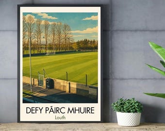 May include: A framed rectangular print featuring a vibrant green sports field under a blue sky with white clouds. Tall bare trees line the background. The text "DEFY PÁIRC MHUIRE" and "Louth" is printed in black at the bottom of the white border.