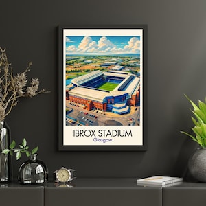 May include: A framed art print of Ibrox Stadium in Glasgow, Scotland. The stadium is depicted in an aerial view with a green field, blue seating, and a blue and white exterior. The sky is blue with fluffy white clouds. The print has the text "IBROX STADIUM Glasgow".