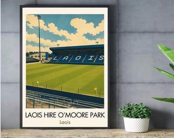 May include: A framed art print depicting a stadium with a green field, blue seating, and a blue sky with white clouds. The text LAOIS HIRE O'MOORE PARK and Laois is printed at the bottom. The stadium features blue stands with the word LAOIS.