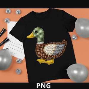 Op de afbeelding: Zwart T-shirt met een patchwork eendenontwerp. De eend heeft een groen-witte geruite kop, een bruin bloemenlichaam en gele voeten. Het ontwerp is gemaakt van verschillende stoffen patches. Het woord "PNG" staat onderaan.