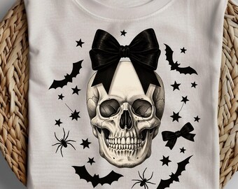 May include: White t-shirt featuring a detailed skull illustration with a large black bow on top. The design includes bats, stars, and spiders, creating a spooky Halloween theme. The word "PNG" is at the bottom.