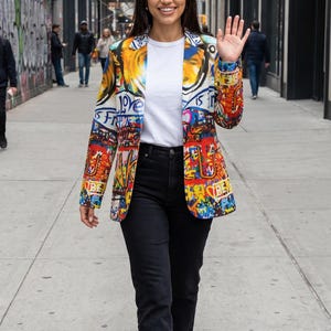 May include: A blazer featuring a vibrant, multi-colored graffiti print with bold text and abstract shapes, worn over a plain white t-shirt and black denim jeans. The blazer has a notched lapel, long sleeves, and a structured fit, paired with white sneakers.