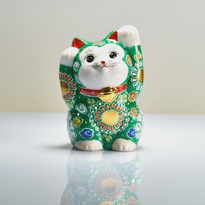 Peut inclure: Une figurine Maneki-neko en céramique verte avec un visage, une poitrine et des pattes blancs. Le chat porte un collier rouge avec une clochette dorée, et son corps est orné de motifs floraux complexes en orange, or, bleu et blanc. Une patte est levée.