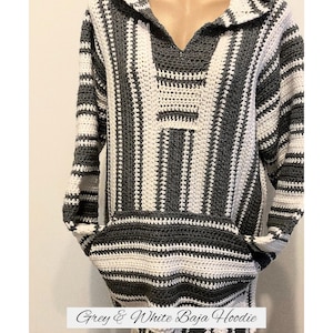 May include: A grey and white Baja hoodie with a v-neck and a front pocket. The long-sleeved sweater is made of a striped crochet pattern. The text "Grey & White Baja Hoodie" is at the bottom of the image.