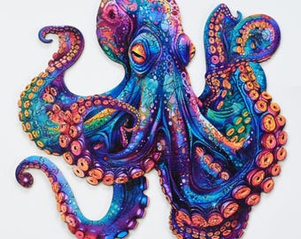 Op de afbeelding: Een kleurrijke houten legpuzzel in de vorm van een octopus. De puzzel heeft levendige tinten blauw, paars, oranje en groen. De octopus heeft gedetailleerde tentakels en ogen, met een complex, artistiek ontwerp. De achtergrond is wit.
