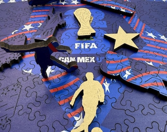 May include: A wooden jigsaw puzzle with soccer-themed pieces. The puzzle features a blue background with white stars and red stripes. Pieces include soccer cleats, a trophy, a star, and soccer player silhouettes. The word "FIFA" is visible.