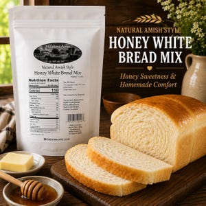 May include: A loaf of honey white bread with two slices cut, displayed on a wooden cutting board. A bag of bread mix and a dish of butter are in the background. The text on the bag reads "Natural Amish Style Honey White Bread Mix."
